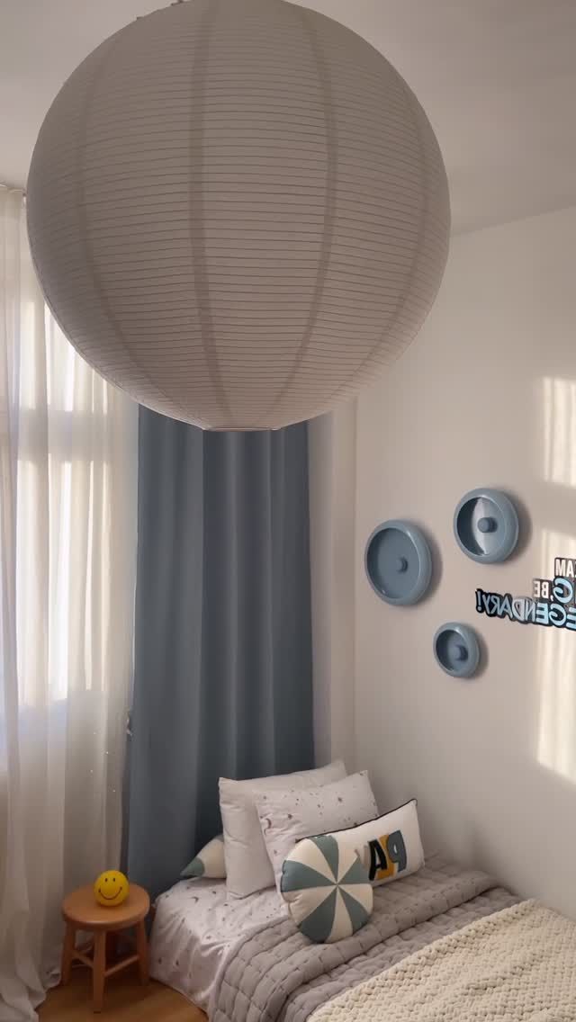 A large paper lantern hangs over a children’s bed with blue wall decorations.
