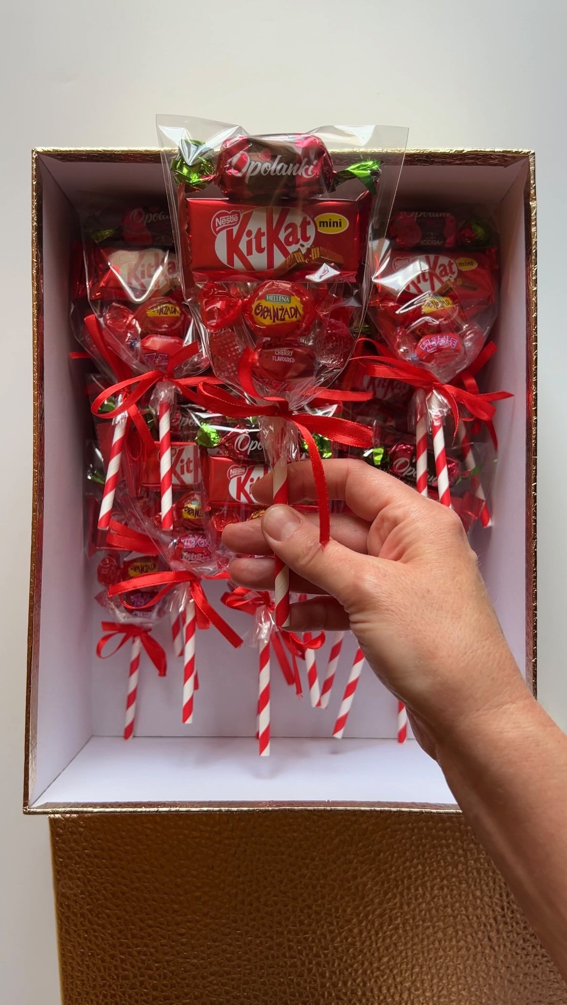 A hand ties a red ribbon around a handmade candy bouquet.