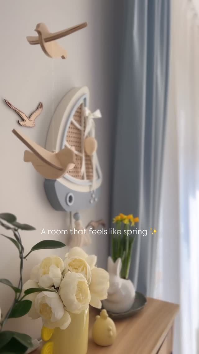 Wooden seagulls hang above a round mirror beside spring flowers.